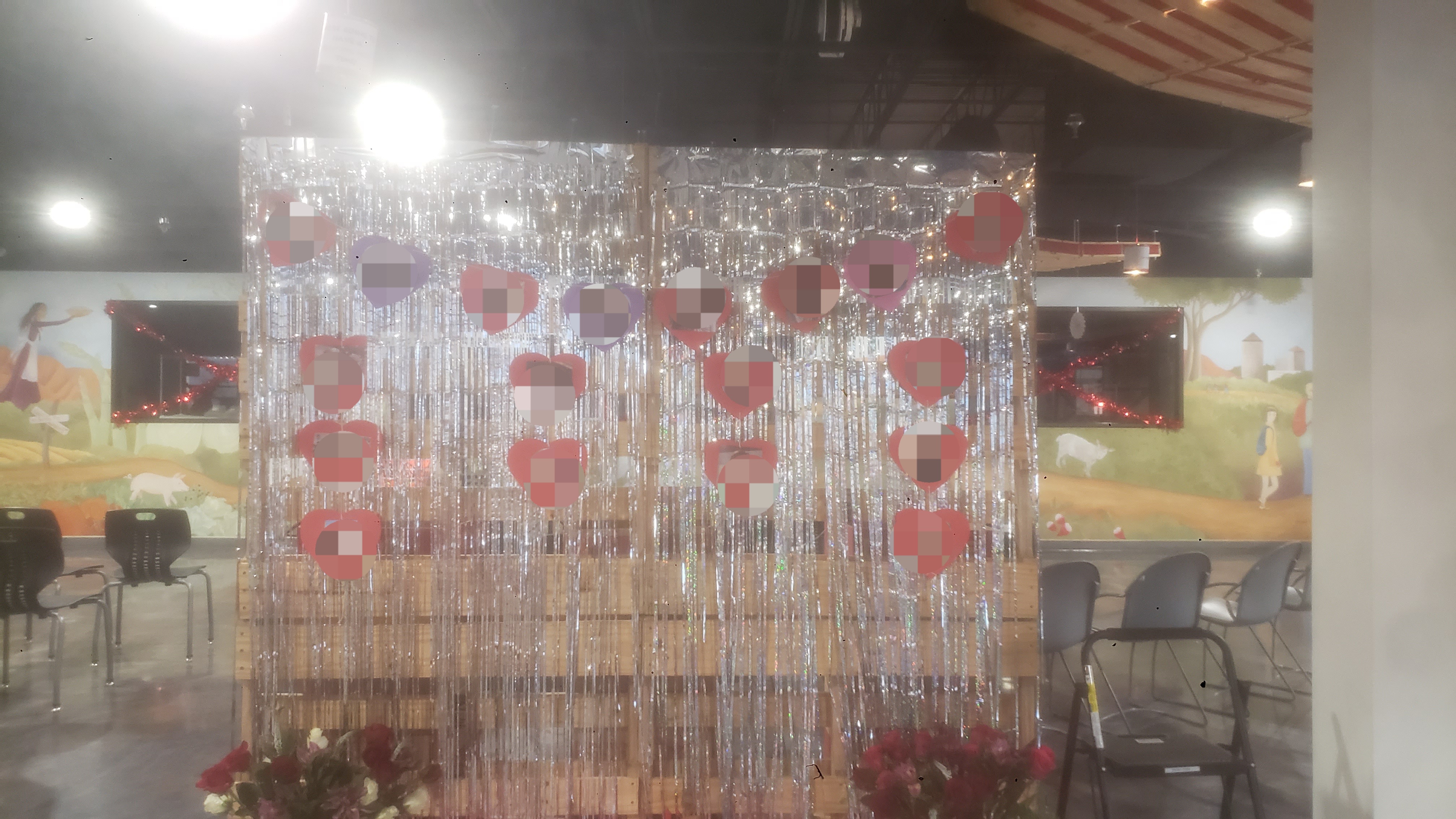 A festive Valentine's Day pallet featuring hanging red hearts with volunteers photos and silver tinsel curtains.